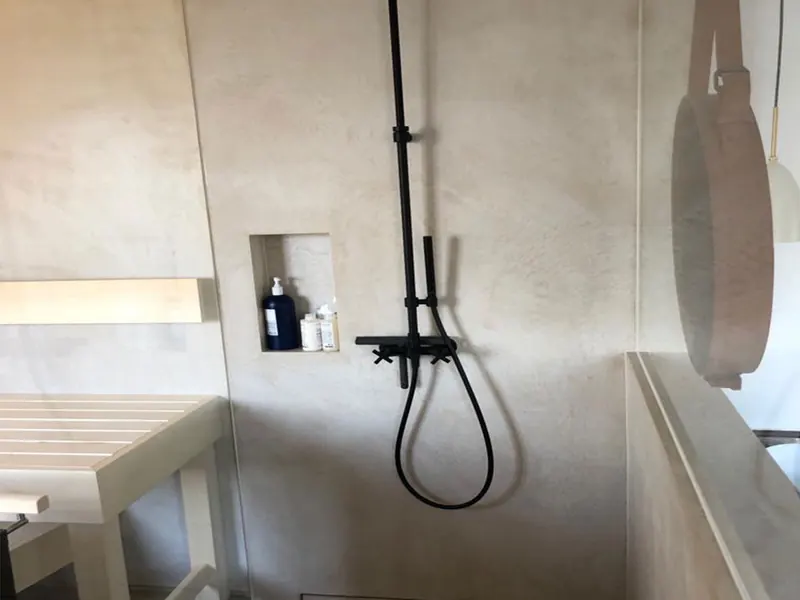 Dusche mit Wandnische und Wänden aus hellem Mikrozement, schwarze Armatur