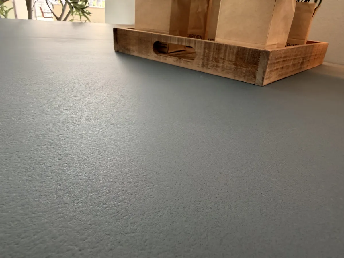 Nahaufnahme einer grauen Mikrozement-Arbeitsplatte mit feiner Struktur, im Hintergrund ein Holztablett