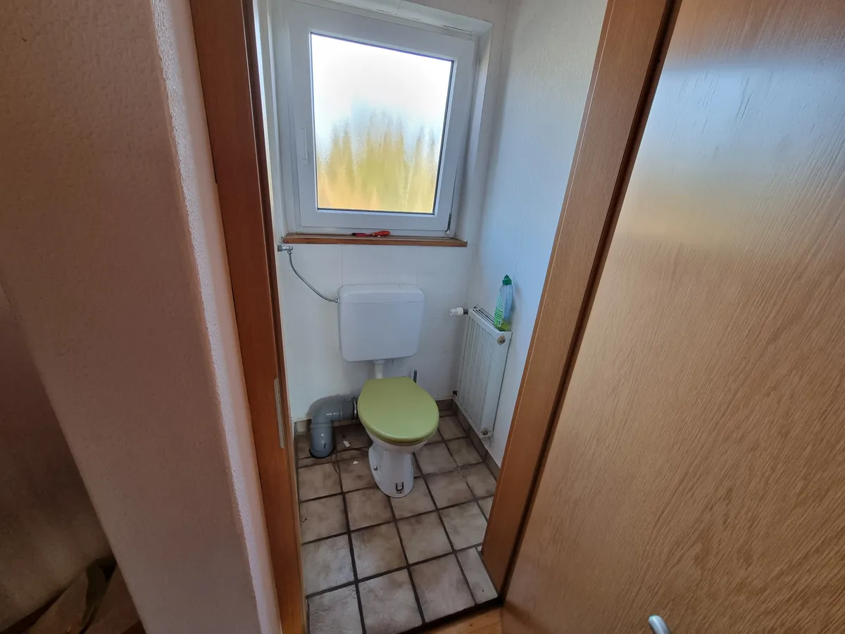 Altes Gäste-WC mit braunen Bodenfliesen und weißen Wandfliesen vor der Renovierung